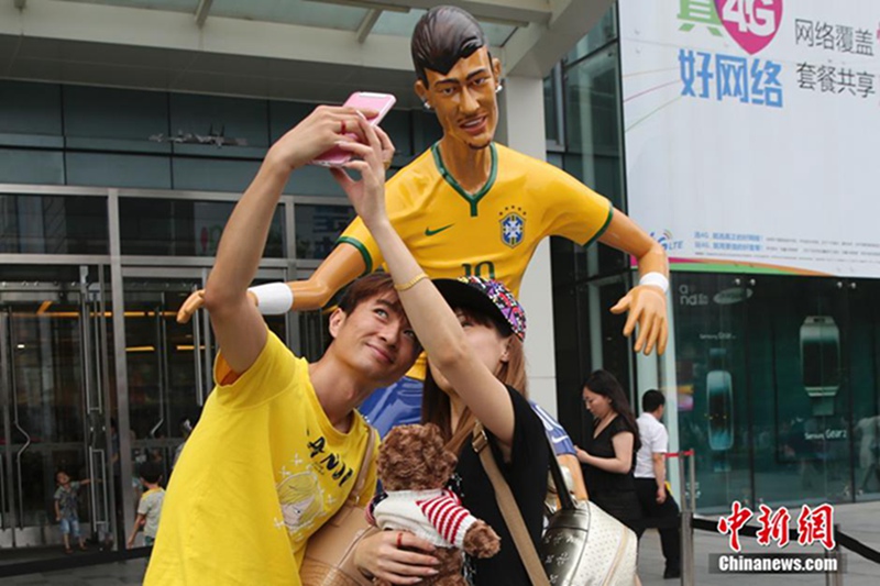 6월 16일, 한 관광객이 베이징 시단(西單)의 한 상점 앞에서 월드컵 축구스타의 모형을 배경으로 사진을 찍고 있다. 중국신문사 슝란(熊然) 촬영기자 