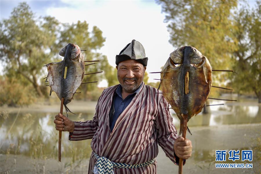 뤄부런(羅布人) 마을, 아무둥•아이부둥(阿木東•艾不東) 씨가 자신이 직접 조리한 생선구이를 선보이고 있다. [2018년 10월 16일 촬영/사진 출처: 신화망]
