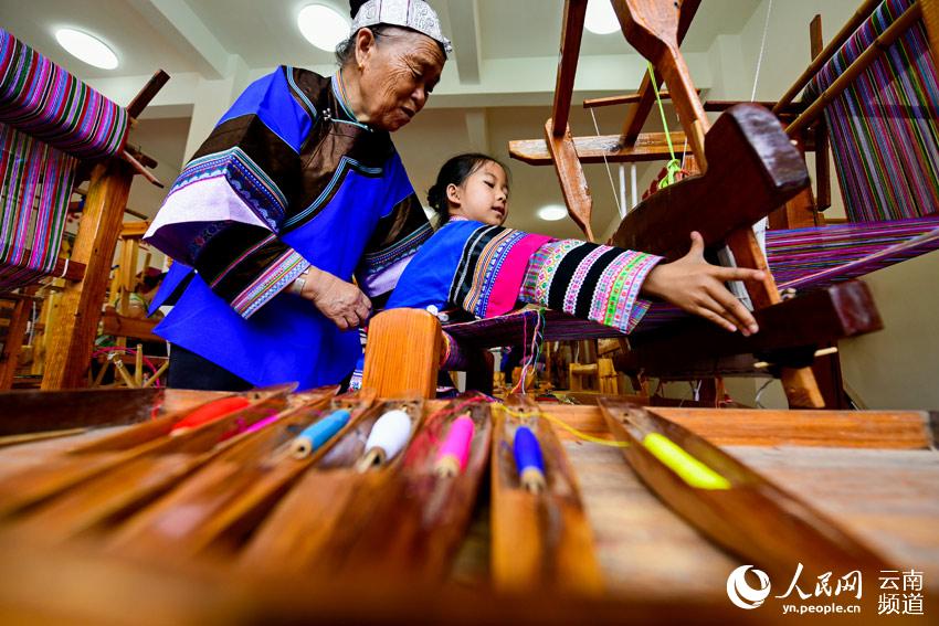 스쭝(師宗)현 우룽(五龍)향 장족(壯族) 비물질문화유산(무형문화재) 계승인과 장족 비단 계승자가 우룽중신(五龍中心)초등학교 학생들에게 장족 비단 만드는 법에 대해 알려주고 있다. [8월 29일 촬영/사진 출처: 인민망]