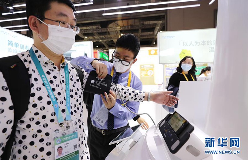 직원(왼쪽 두 번째)이 관람객을 도와 혈압계를 체험하고 있다. 이 제품은 스마트폰과 연결하게 혈압과 심전도를 동시에 체크할 수 있다. [사진 출처: 신화망]