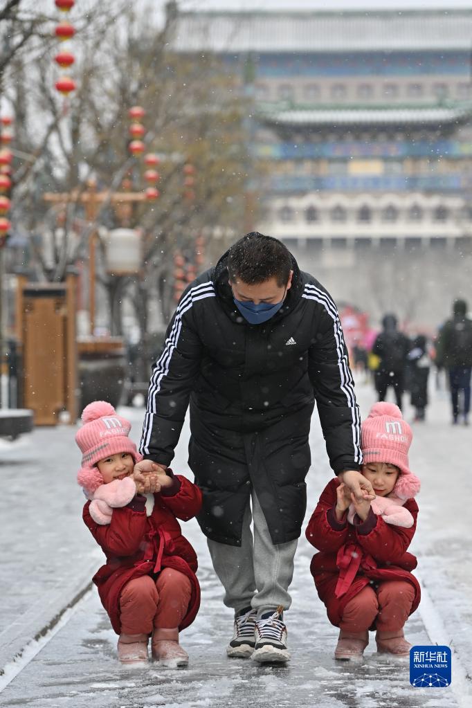 베이징 첸먼다제에서 쌍둥이 자녀를 둔 남성이 아이들과 눈 속에서 놀고 있다. [사진 출처: 신화사]