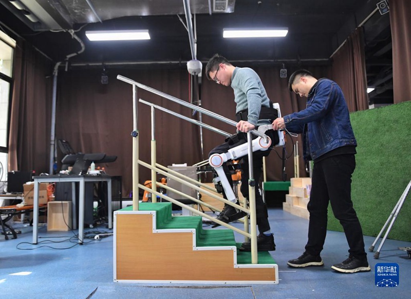 3월 6일, 연구원의 도움으로 하반신 마비환자가 외골격 로봇의 계단 오르내리기 재활훈련 기능을 체험 중이다. [사진 출처: 신화사]