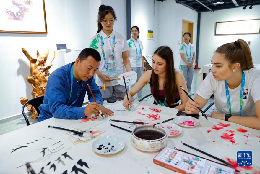 선수촌에서 쓰촨 사범대학교 미술대 자오하이룽(焦海龍) 부교수(앞 왼쪽)는 에스토니아 선수 아델리나(앞 가운데)와 한나(앞 오른쪽)에게 중국화 그리는 법을 선보인다. [7월 31일 촬영/사진 출처: 신화사]