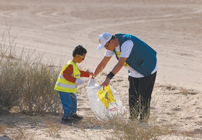 2023년 12월 5일부터 16일까지 열린 제22회 ‘클린 아랍에미리트’(Clean UAE) 공익 환경보호 행사에서 아랍에미리트 주재 중국 투자 기관 자원봉사자 100여 명이 주변 환경을 개선하고 더 많은 사회적 역량이 녹색 환경보호에 관심을 가지도록 유도하며 친환경 생태의 지구 환경을 만드는 데 기여하길 바라는 마음으로 현지 자원봉사자와 함께 두바이 알 마르뭄(Al Marmoom) 사막 보존구역에서 사막의 쓰레기를 치웠다. 한 중국 기관 자원봉사자의 지도 아래 어린이가 주운 쓰레기를 마대 자루에 담고 있다. [사진 출처: 인민일보]