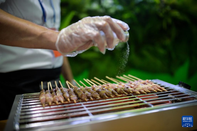 6월 26일, 우루무치에 위치한 신장국제컨벤션센터의 신장농축산업투자 업체 전시부스에서 직원이 양꼬치 바비큐를 선보이고 있다.