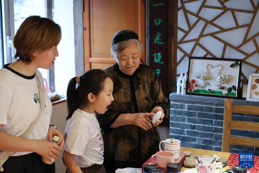 류안친 씨는 어린이에게 자신의 돌그림을 소개한다. [8월 4일 촬영/사진 출처: 신화사]